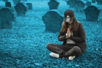 Mädchen mit Adidas-Mütze sitzt auf einem Friedhof und betet.